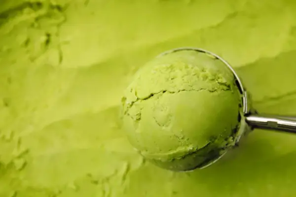 Eine Kugel cremiges Matcha-Eis wird mit einem Löffel aus einer Schüssel gehoben. Perfekt für ein erfrischendes Matcha Eis Rezept.