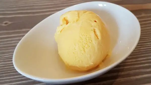 Ein Löffel cremiges, gelbes balla balla Eis in einer weißen Schale auf Holzhintergrund.