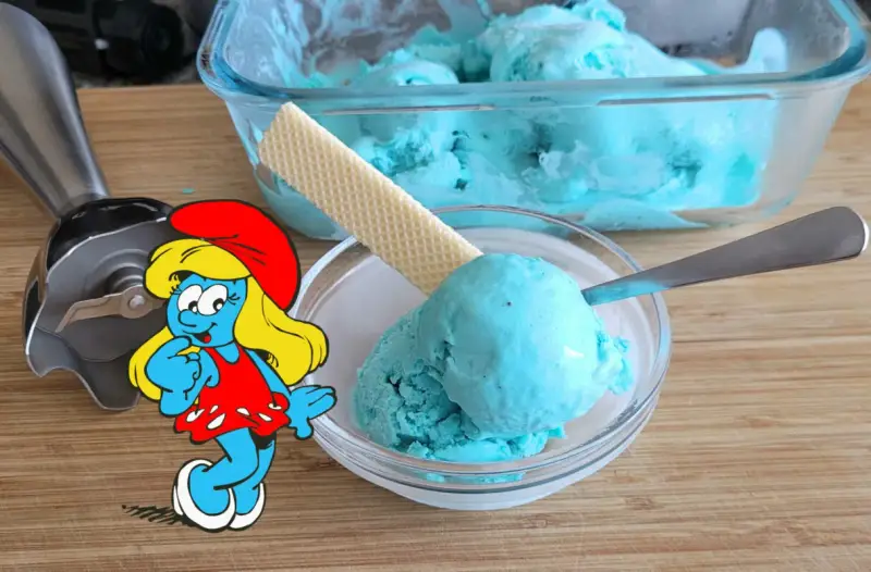 Schlumpfine genießt engelblaues Eis. Ein Handmixer und ein Waffelblatt liegen daneben.