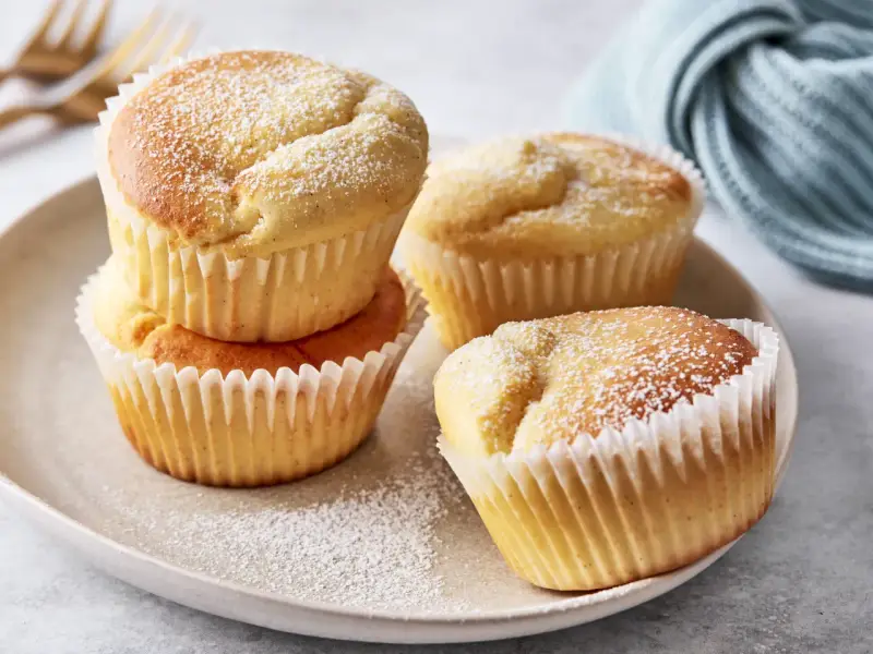 Saftige Quark Muffins, bestäubt mit Puderzucker, auf einem Teller.